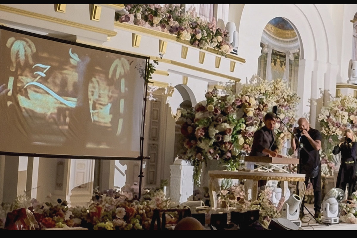 Bilal Köse performing live sand art at a wedding, the artwork projected on a large screen beside the stage